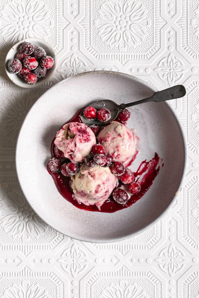 three scoops of homemade dairy free cranberry swirl ice cream in a bowl with a spoon topped with sugared cranberries