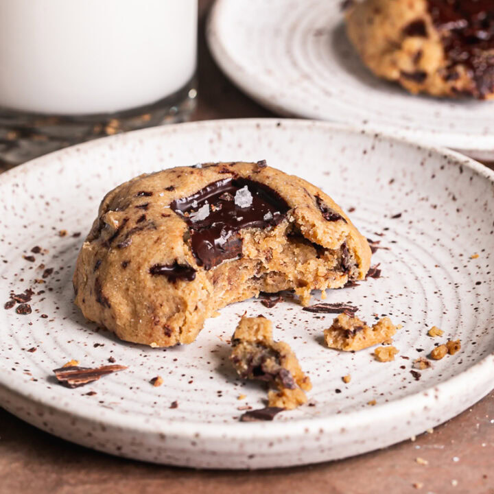 a 3/4 image of a Small batch peanut butter chocolate chunk air fryer cookie on a plate with a bite taken out if it and another cookie on a separate plate in the background with a glass of almond milk