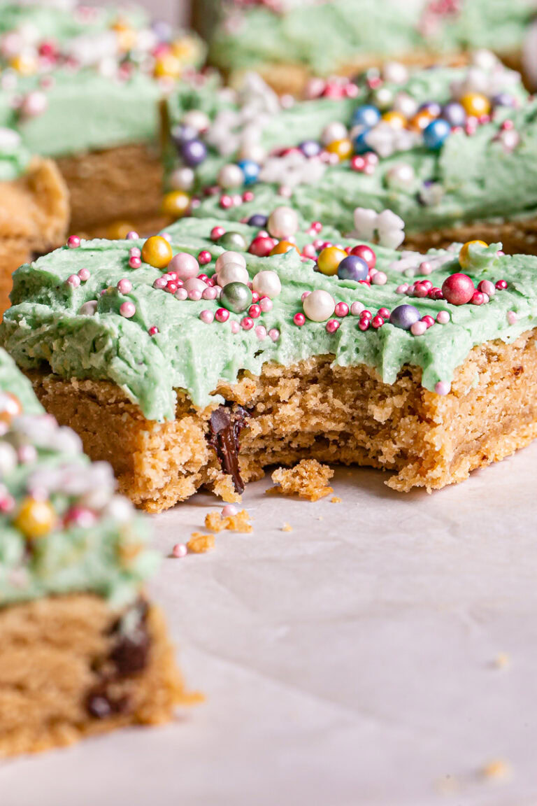 a close up shot of a vegan gluten free frosted cookie dough square with a bite taken out of it
