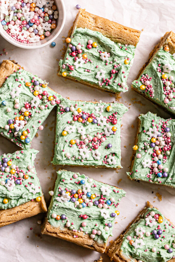 overhead shot of green frosted cookie bars decorated with sprinkles cut into squares with a bowl of sprinkles