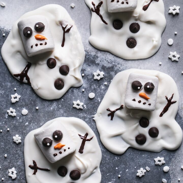 four melted white chocolate snowmen with snowman sprinkles around it