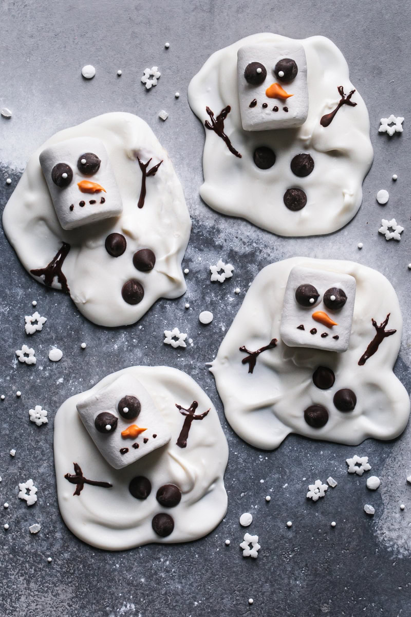 four melted white chocolate snowmen with snowman sprinkles around it