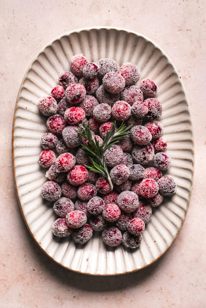 sugared cranberries on a plate topped with a sprig of rosemary