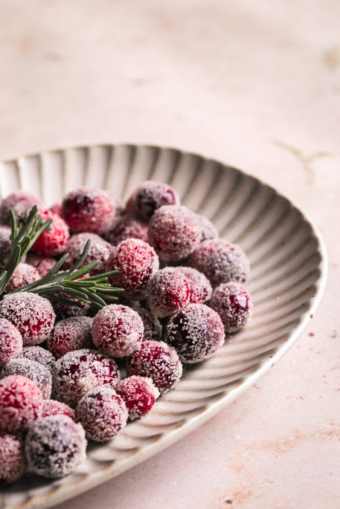 close up of sugared cranberries on a plate with a sprig of rosemary