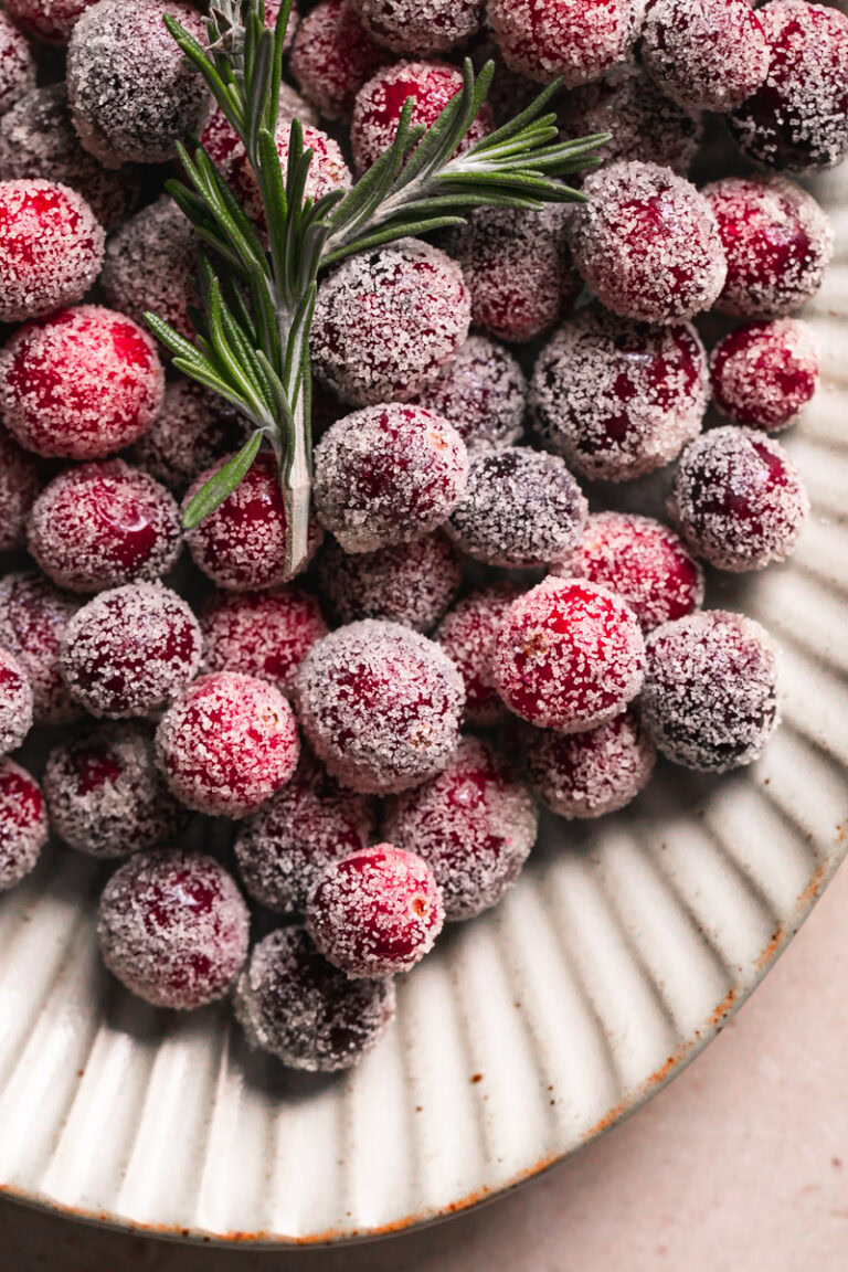 close up of sugared cranberries on a plate with a sprig of rosemary