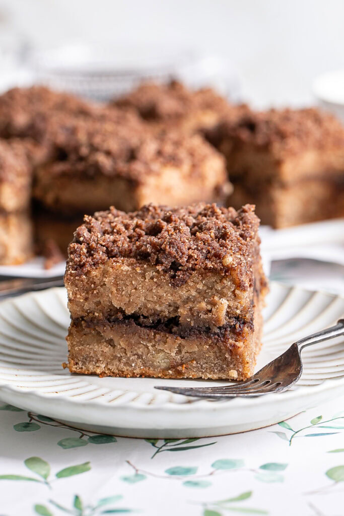 a piece of coffee cake on a plate with a fork and the other slices of coffee cake in the background