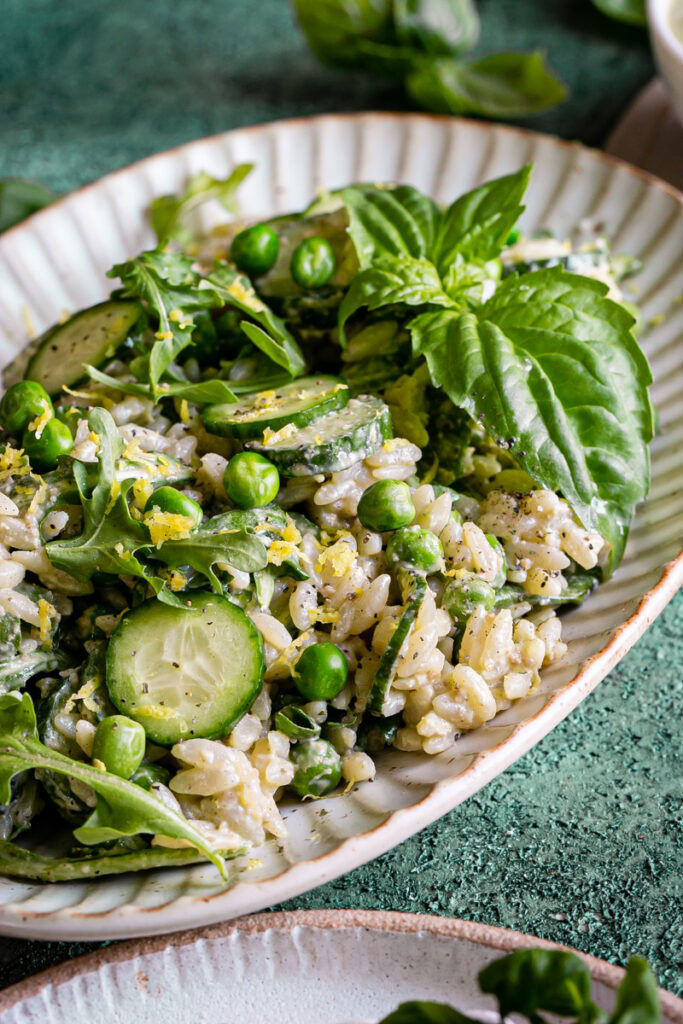 a close up of lemon basil orzo salad with peas, cucumber, and arugula on an oval plate garnished with fresh basil