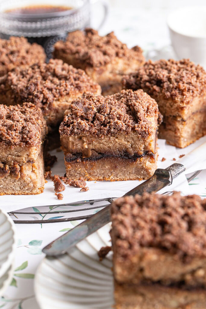 almond flour coffee cake sliced into squares on a parchment lined wire cooking rack, one piece on a plate with a butter knife