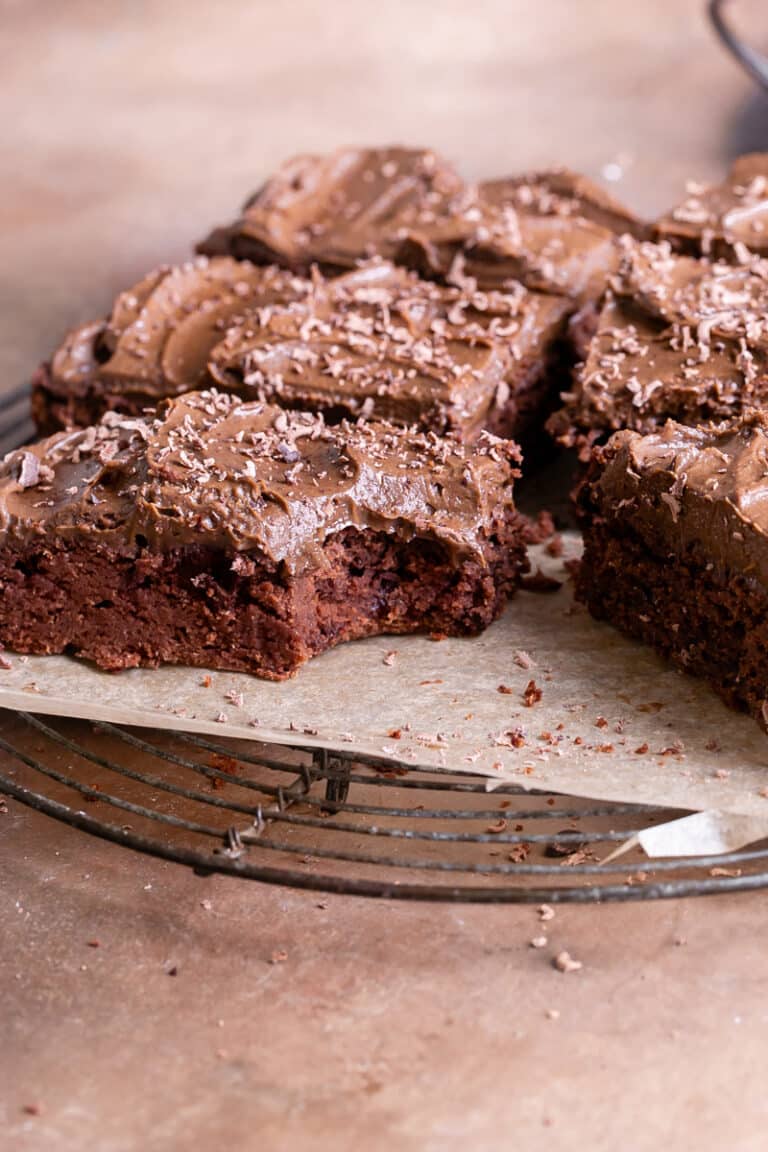 butternut squash brownies on a parchment lined wire cooling rack topped with chocoalte avocado frosting, one brownie with a bite taken out of it