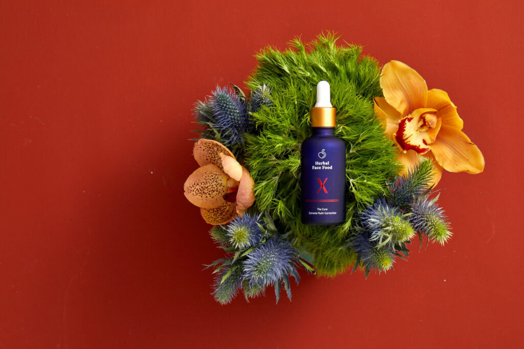 a bottle of herbal face food the cure x serum laying on top of exotic plants