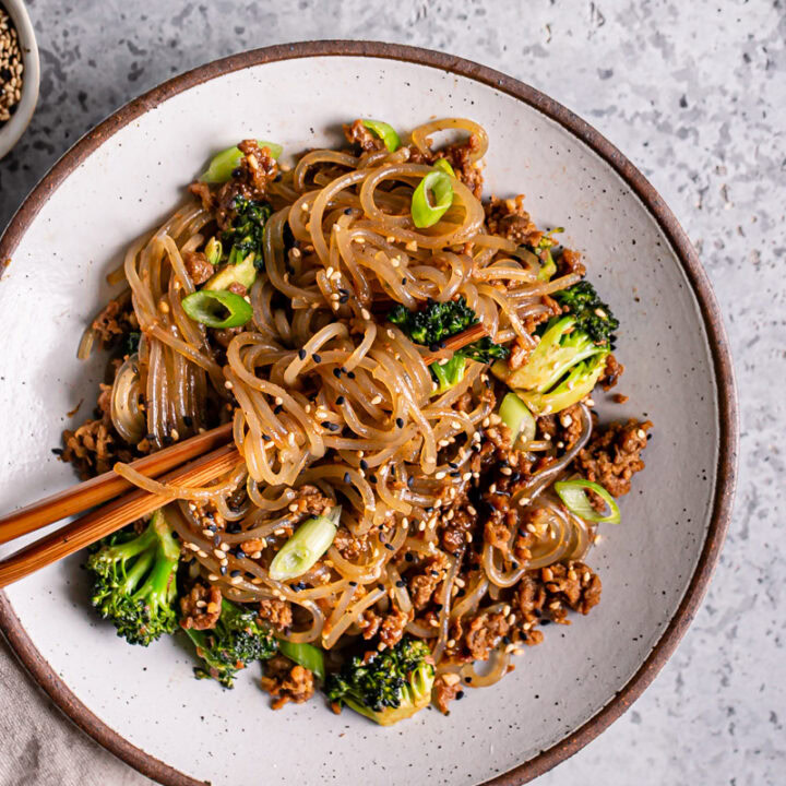 a close up of one bowl of vegan beef and broccoli teriyaki noodles with noodles twirled around the chopsticks