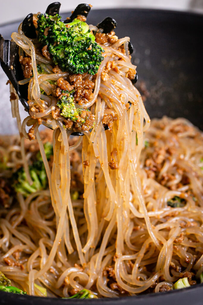 scooping out the noodles with plant based beef and broccoli teriyaki with a spaghetti spatula