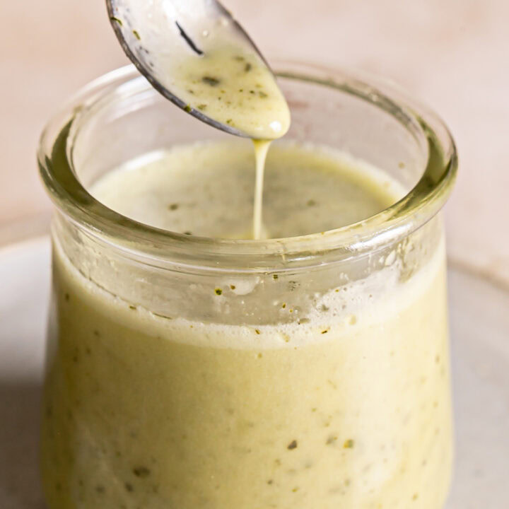 close up of a jar of lemon basil vinaigrette dressing with a spoon drizzling some dressing back into the jar