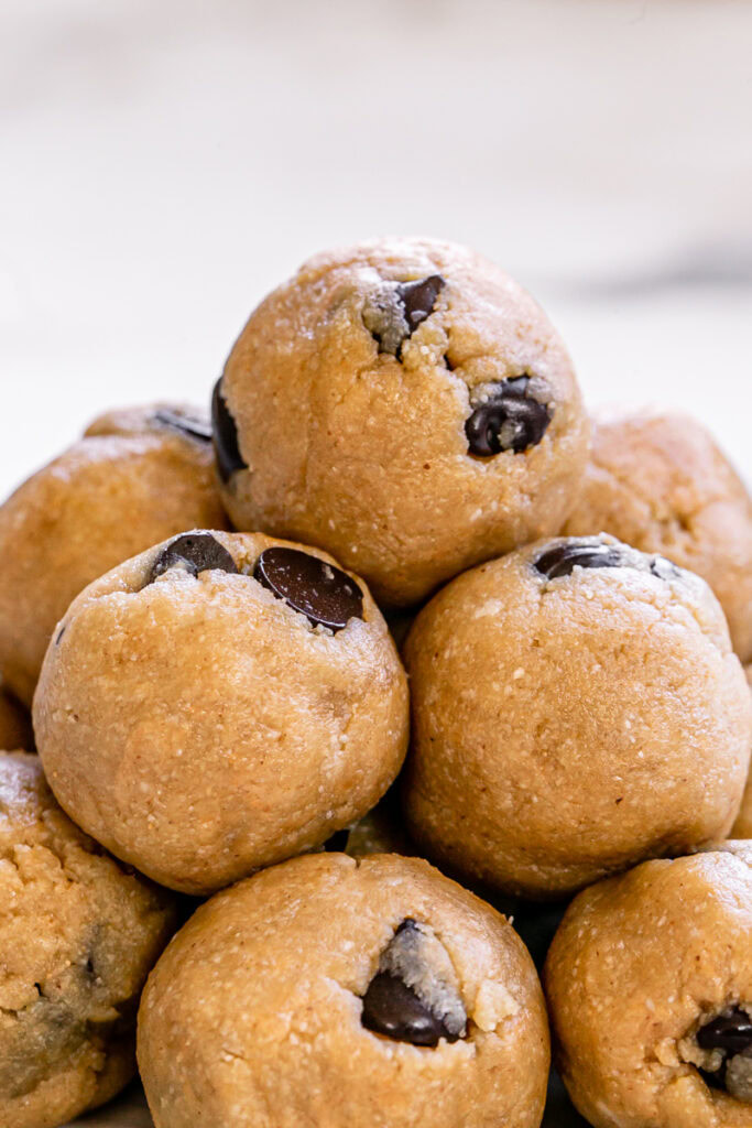 a close up of almond flour chocolate chip cookie dough bites piled on top of one another on a plate