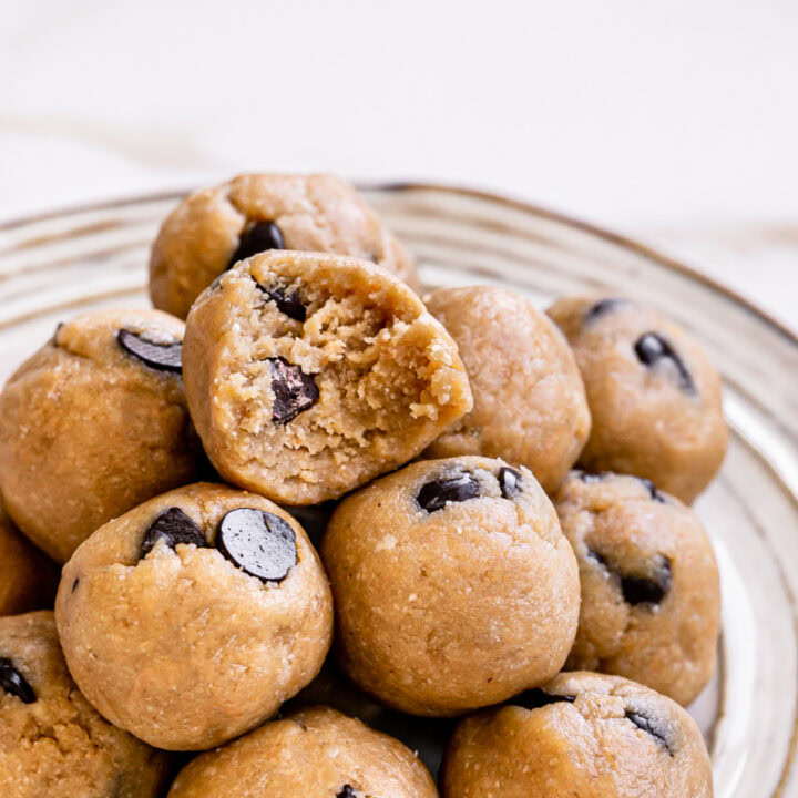 almond flour chocolate chip cookie dough bites piled on top of one another on a plate with a bite taken out of the top one