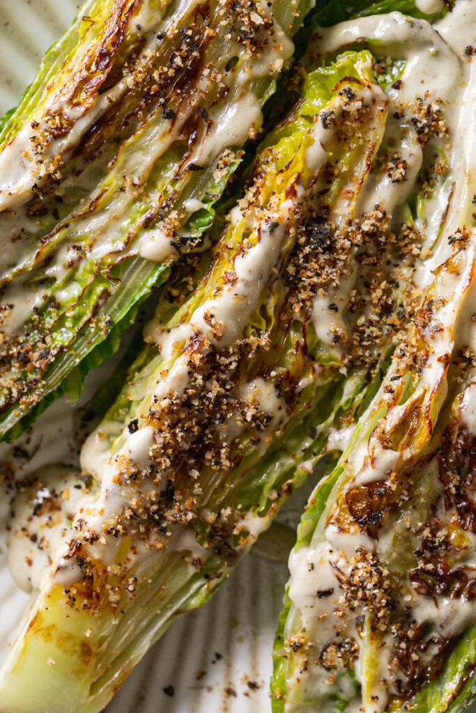 close up overhead shot of three halves of romaine lettuce drizzled with vegan caesar dressing and sprinkled with grain-free breadcrumbs