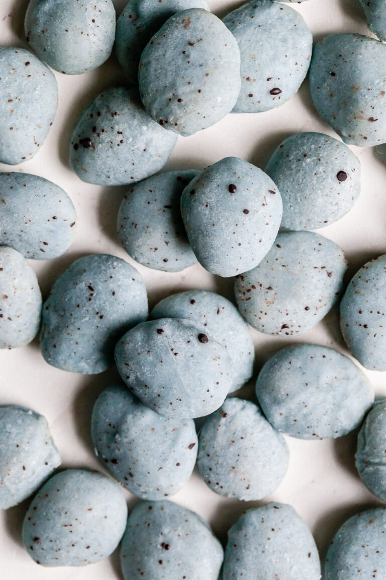 a pile of white chocolate covered almonds colored robin's egg blue using blue spirulina and speckled with dark chocolate.