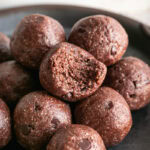 a close up of Sunflower seed chocolate brownie bites rolled and stacked on a round metal plate, the top bite with a bite taken out of it.