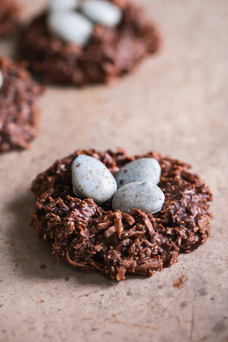 3/4 shot of a Toasted Coconut Chocolate Bird's Egg Nest Cookie filled with three robin's egg white chocolate covered almonds in it and other cookies in the background