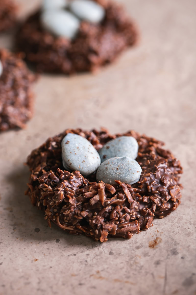 3/4 shot of a Toasted Coconut Chocolate Bird's Egg Nest Cookie filled with three robin's egg white chocolate covered almonds in it and other cookies in the background