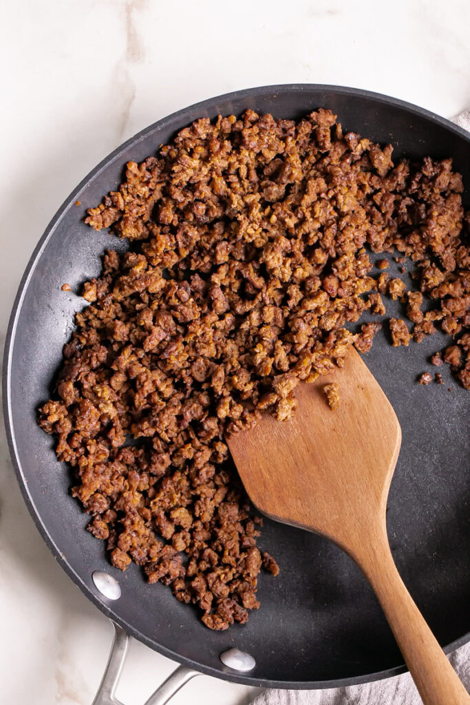 cooked plant based ground beef in a skillet with a wooden spatula in it