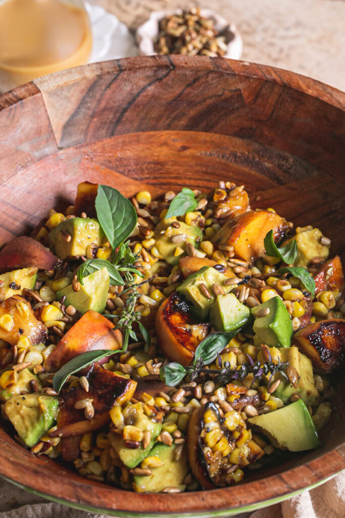 a 3/4 close up shot of Grilled Corn Peach Avocado Salad with Orange Ginger Miso Dressing in a wooden bowl