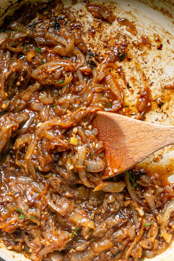 caramelized onions in a large skillet with a wooden spoon in the skillet