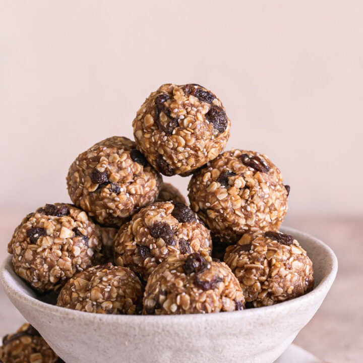 a close up shot of No-Bake Oatmeal Raisin Protein Cookie Dough Bites piled on top of each other in a bowl