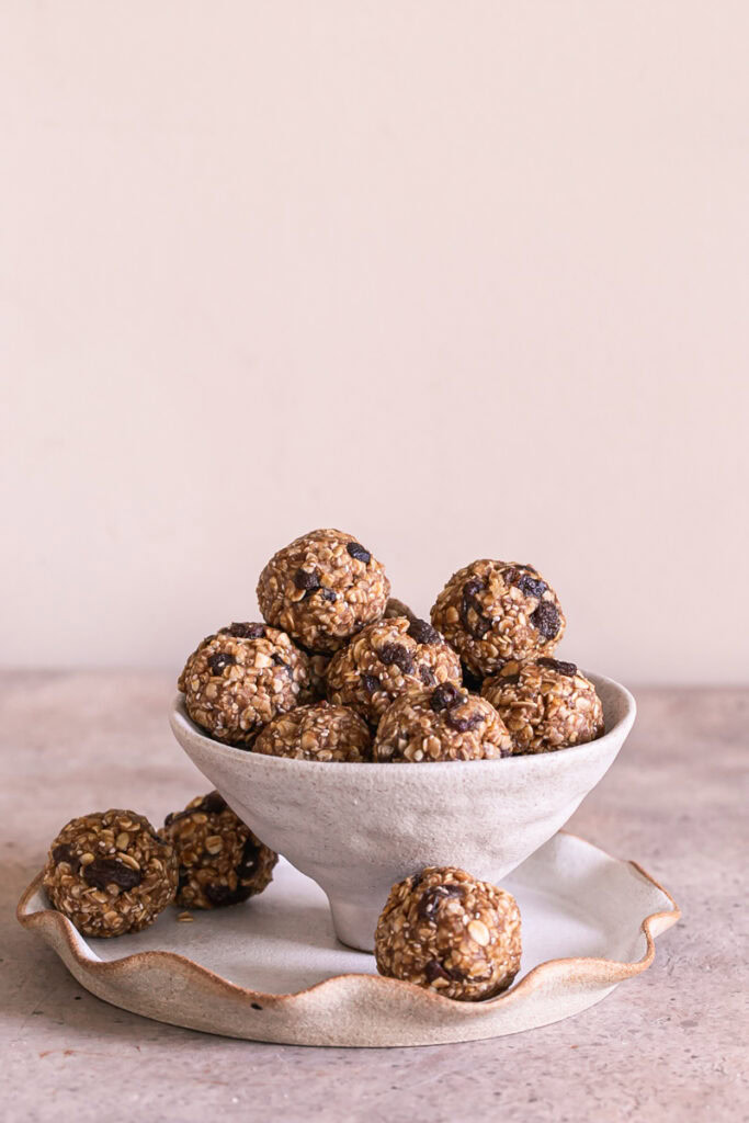 No-Bake Oatmeal Raisin Protein Cookie Dough Bites in a bowl sitting on a plate with 3 bites on the plate next to the bowl