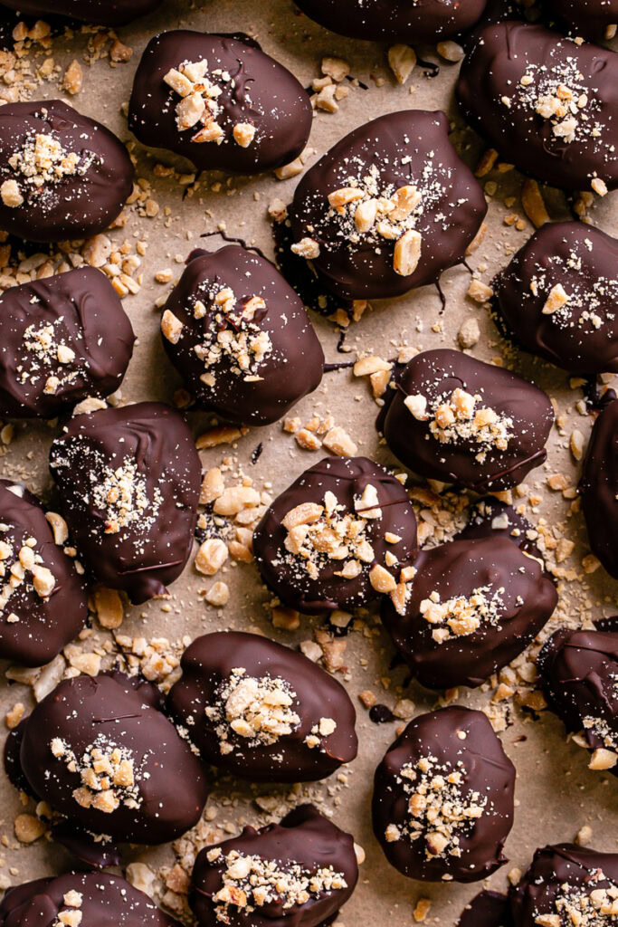 "Snickers" Frozen Yogurt Chocolate Covered Date Bites on a parchment lined baking sheet garnished with chopped peanuts