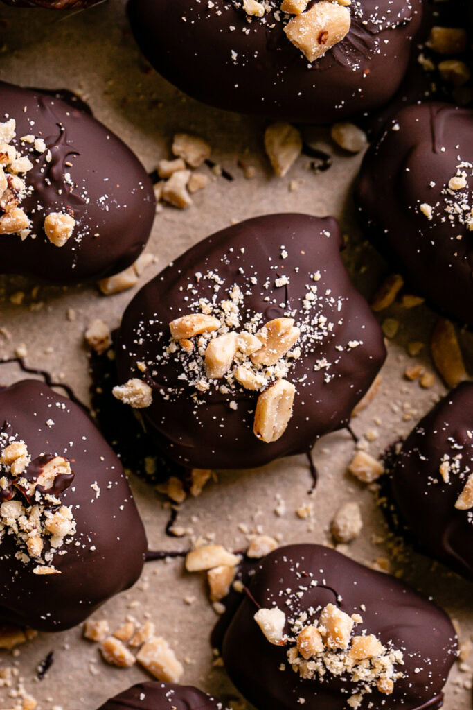 close up of "Snickers" Frozen Yogurt Chocolate Covered Date Bites on a parchment lined baking sheet garnished with chopped peanuts