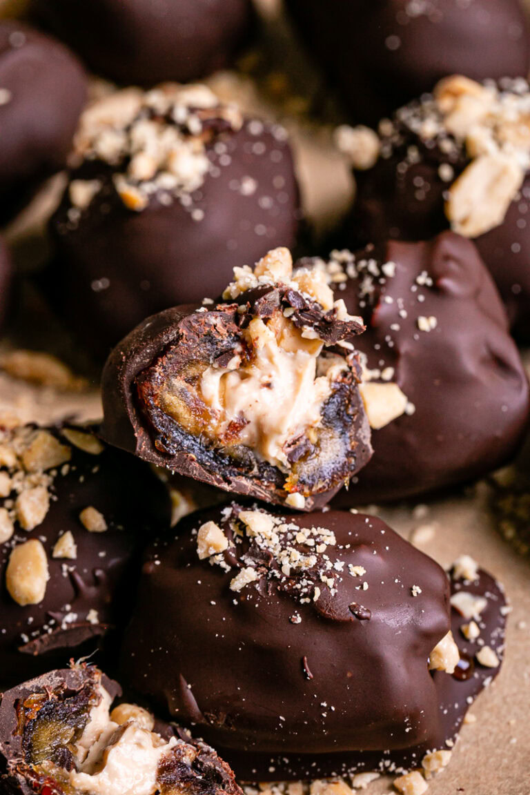 "Snickers" Frozen Yogurt Chocolate Covered Date Bites on a parchment lined baking sheet, one cut in half to reveal the peanut butter yogurt filling