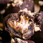 a close up of "Snickers" Frozen Yogurt Chocolate Covered Date Bites on a parchment lined baking sheet, one cut in half to reveal the peanut butter yogurt filling