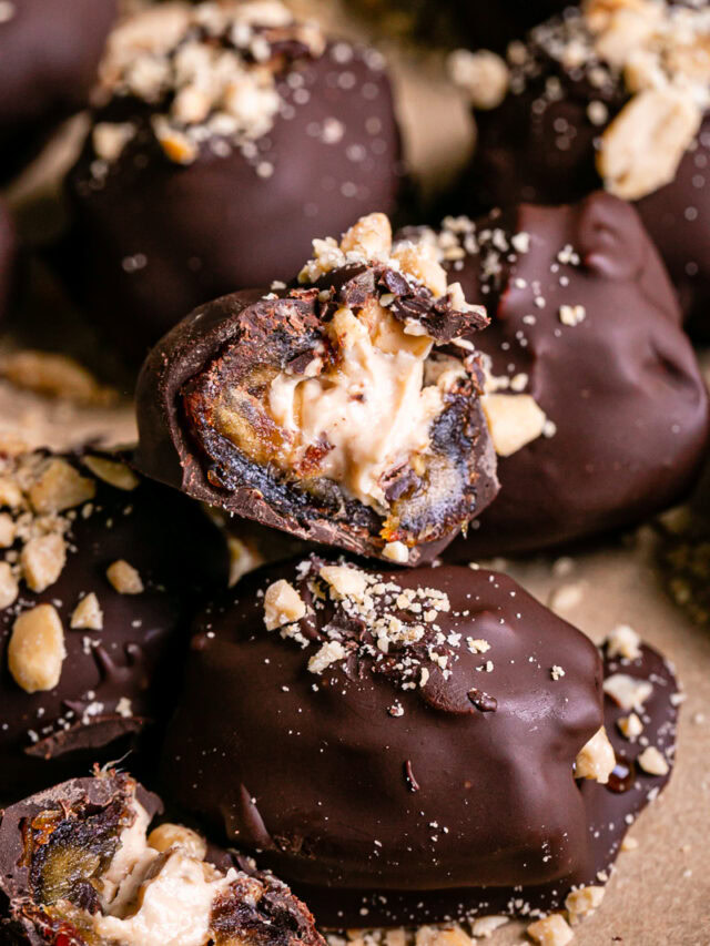 "Snickers" Frozen Yogurt Chocolate Covered Date Bites on a parchment lined baking sheet, one cut in half to reveal the peanut butter yogurt filling