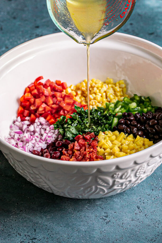 action shot of pouring the apple cider vinegar dressing into the large bowl with all of the bean dip ingredients 