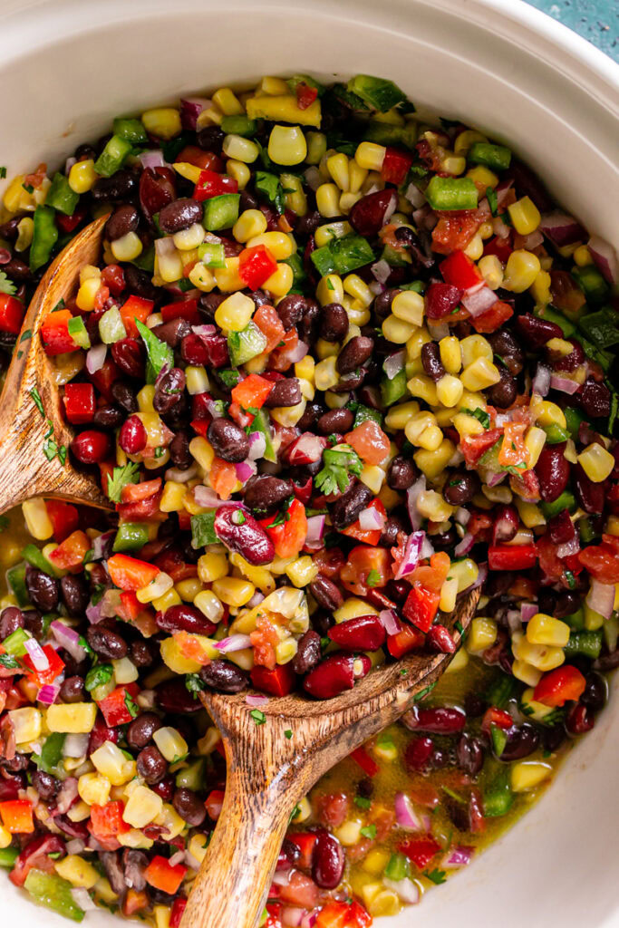 all of the cowboy caviar bean dip ingredients tossed together with the dressing with salad servers in the bowl