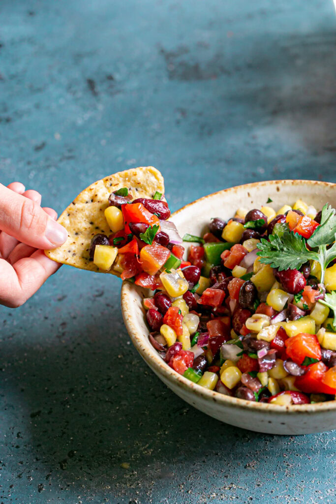 action shot of a hand scooping some of the bean dip onto a tortilla chip