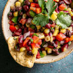 a bowl of cowboy caviar bean dip garnished with fresh cilantro with two tortilla chips sticking out of the bowl, one with bean dip scooped onto the chip.