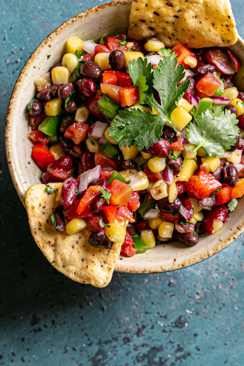 a bowl of cowboy caviar bean dip garnished with fresh cilantro with two tortilla chips sticking out of the bowl, one with bean dip scooped onto the chip.
