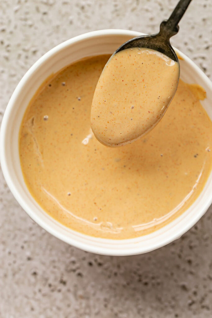 a bowl of harissa tahini sauce with a spoon full of the sauce coming out of the bowl