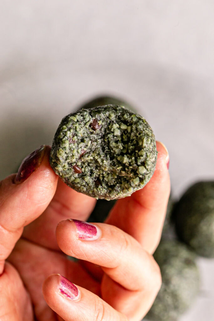 a hand holding a Spirulina Pumpkin Seed Chocolate Chip Bite with a bite taken out of it 