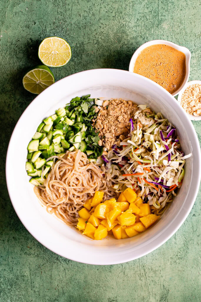 all of the Thai Peanut Glass Noodle Salad ingredients in a large bowl with the dressing in a small bowl and lime wedges above it