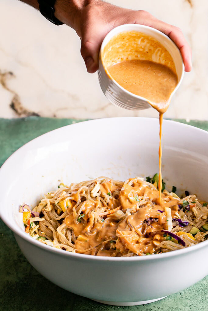 action shot of pouring the Thai peanut dressing into the bowl with the noodles and other salad ingredients