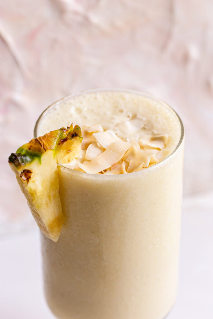 a close up shot of 5-Ingredient Pina Colada Smoothie garnished with a fresh slice of pineapple and coconut chips