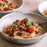 3/4 shot of 3 bowls of Cherry Tomato Puttanesca spaghetti with a glass of wine in the background