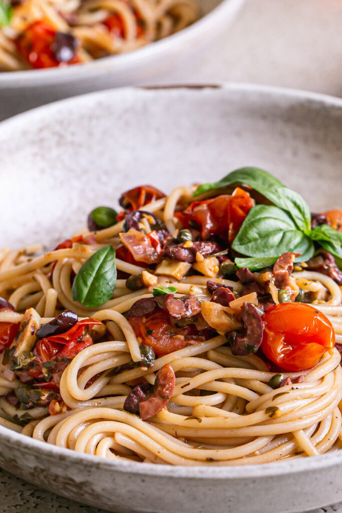 close up 3/4 shot of a bowl of Cherry Tomato Puttanesca garnished with fresh basil leaves