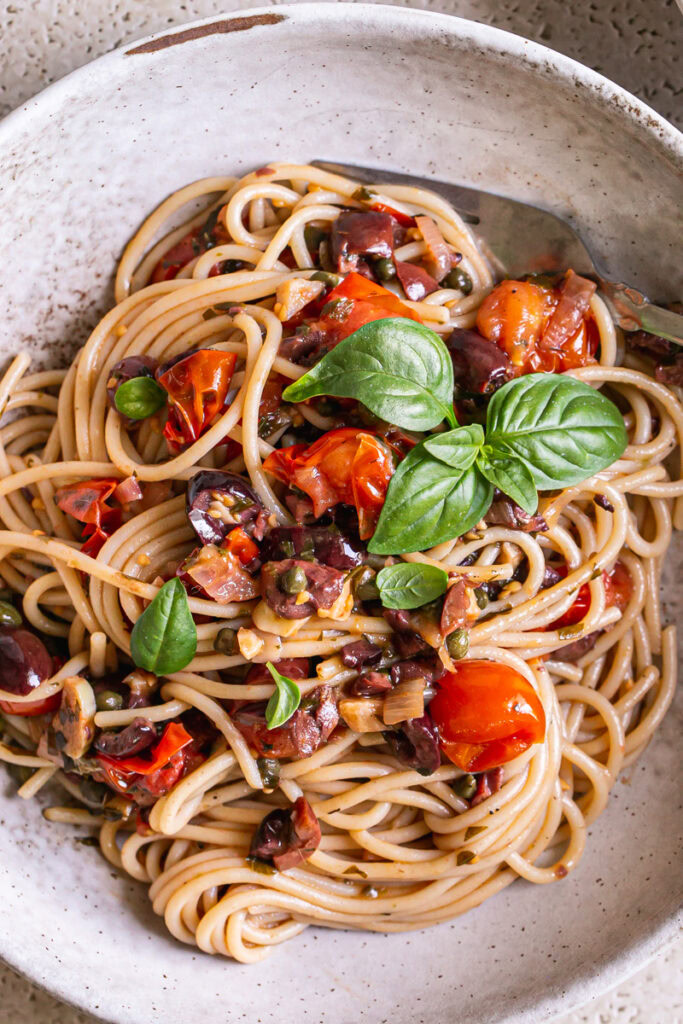 close up shot of a bowl of Cherry Tomato Puttanesca garnished with fresh basil leaves