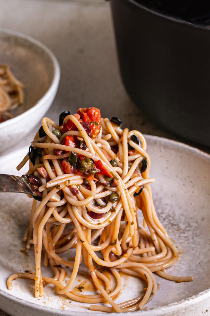 action shot of placing the scoop of spaghetti cherry tomato puttanesca into a pasta bowl