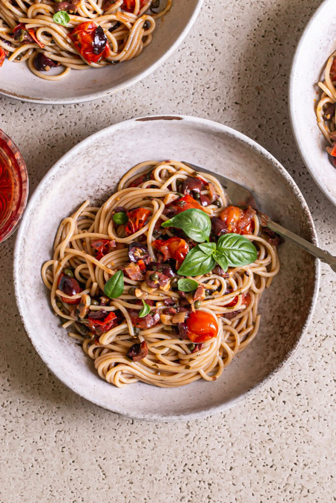 three bowls of Cherry Tomato Puttanesca garnished with fresh basil leaves and a fork in one of the bowls