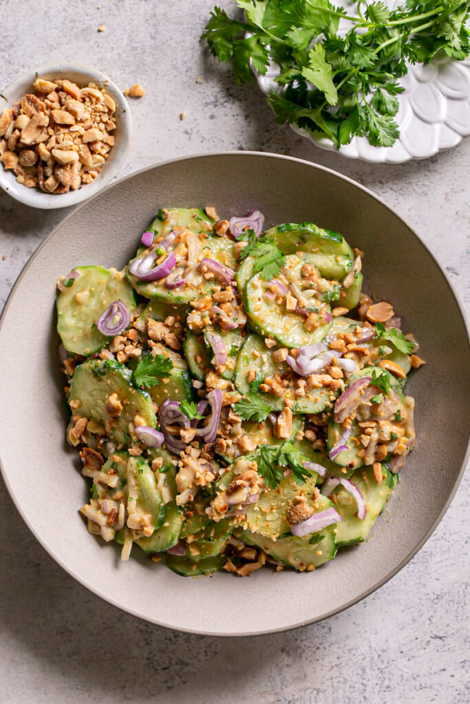 a bowl of Miso Cucumber Salad with Shallot and Roasted Peanuts and a small plate of fresh cilantro and a bowl of crushed roasted peanuts above it